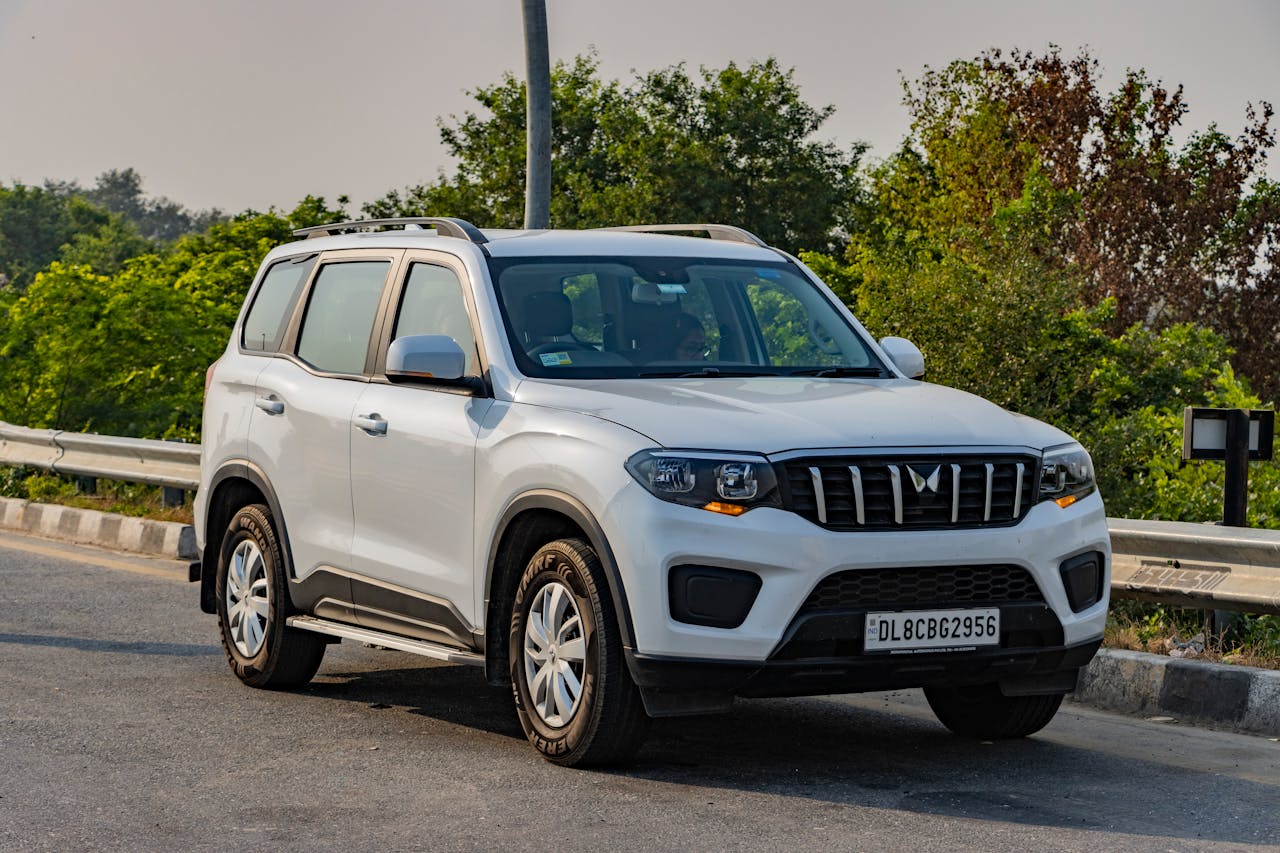 White Mahindra SUV parked on a highway in Deeg, India, surrounded by lush greenery.